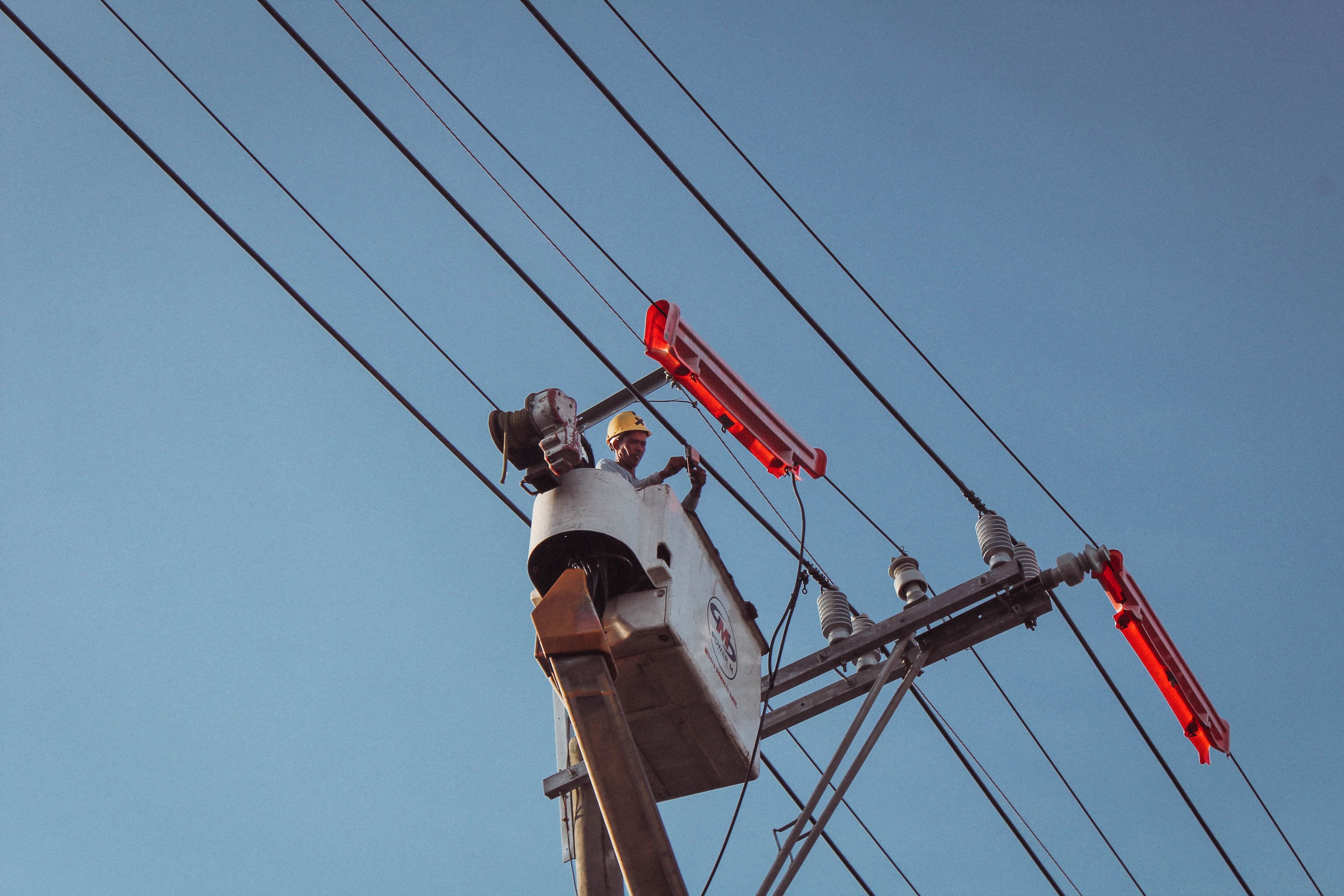 Electrician in a lift repairing overhead power lines on a clear day.