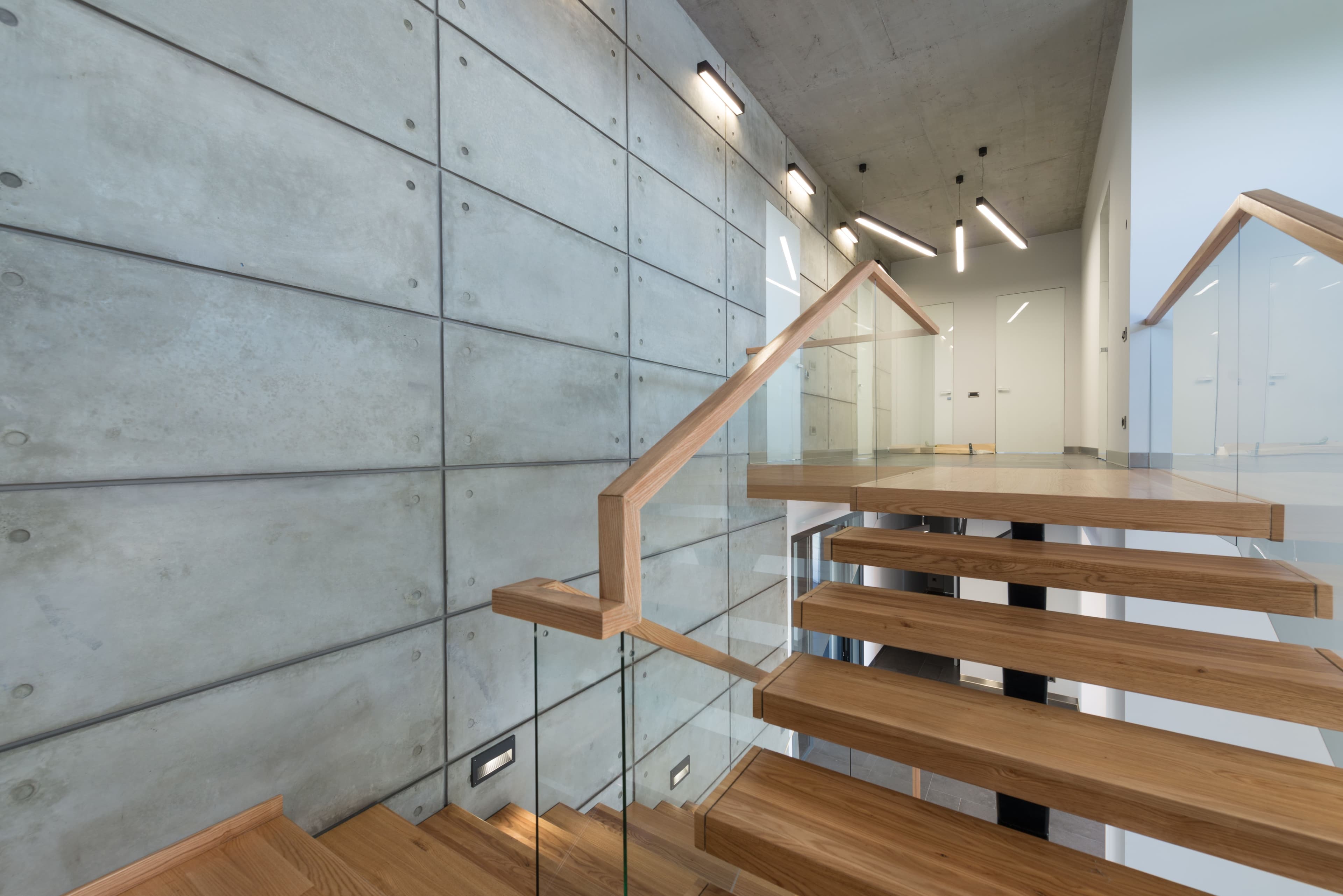 Interior of empty contemporary house hallway with wooden flight of stairs and glass banister