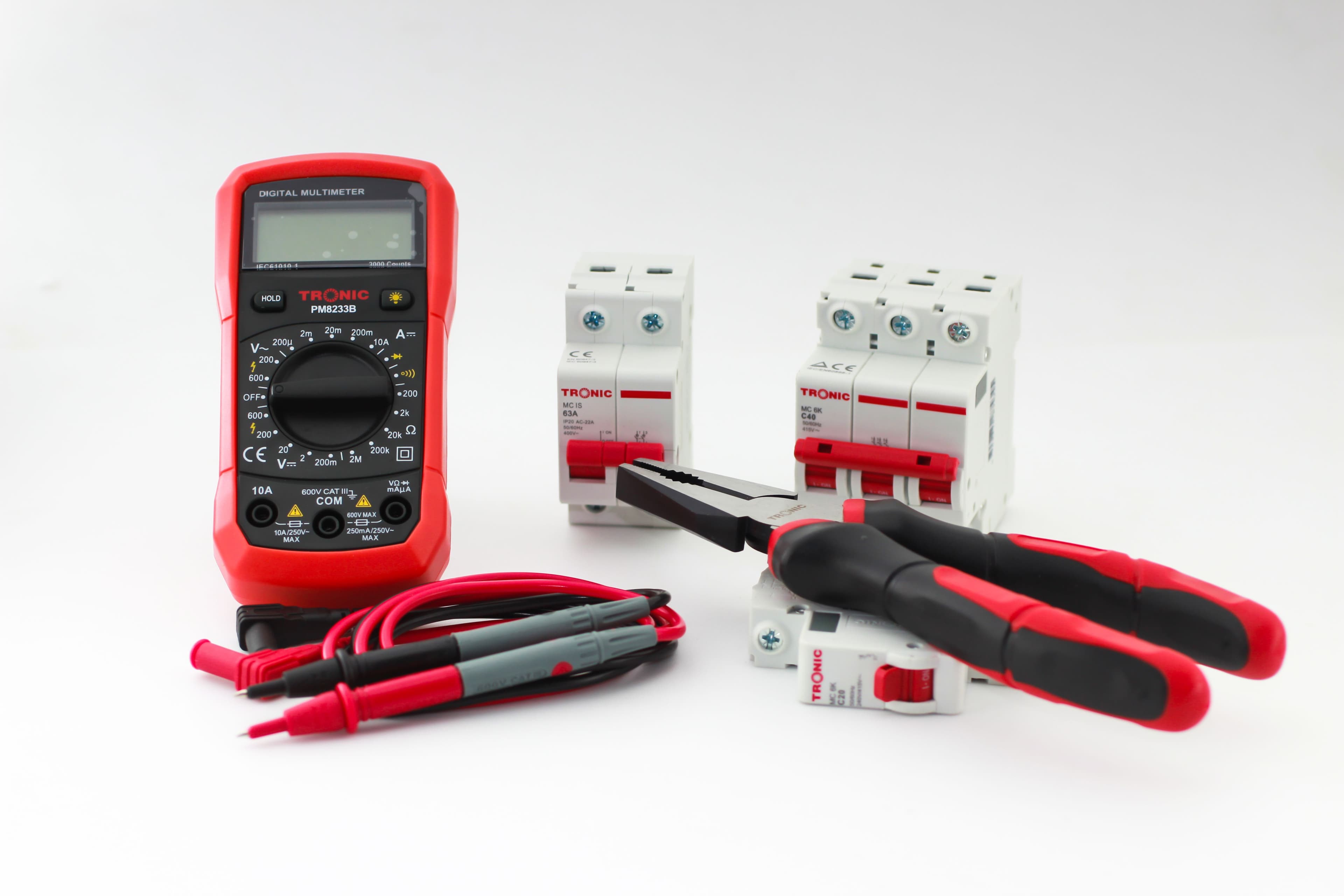 Close-up of a digital multimeter with electrical tools and circuit breakers on a white background.