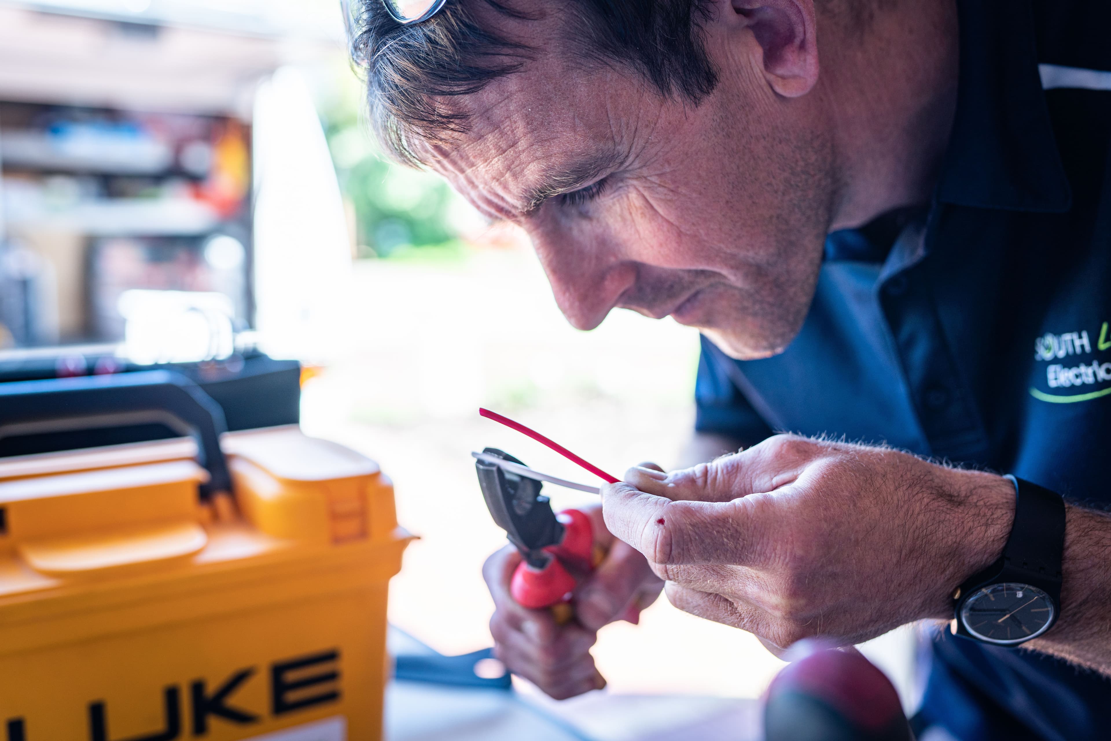 Focused technician working on wiring with tools in a workshop setting.