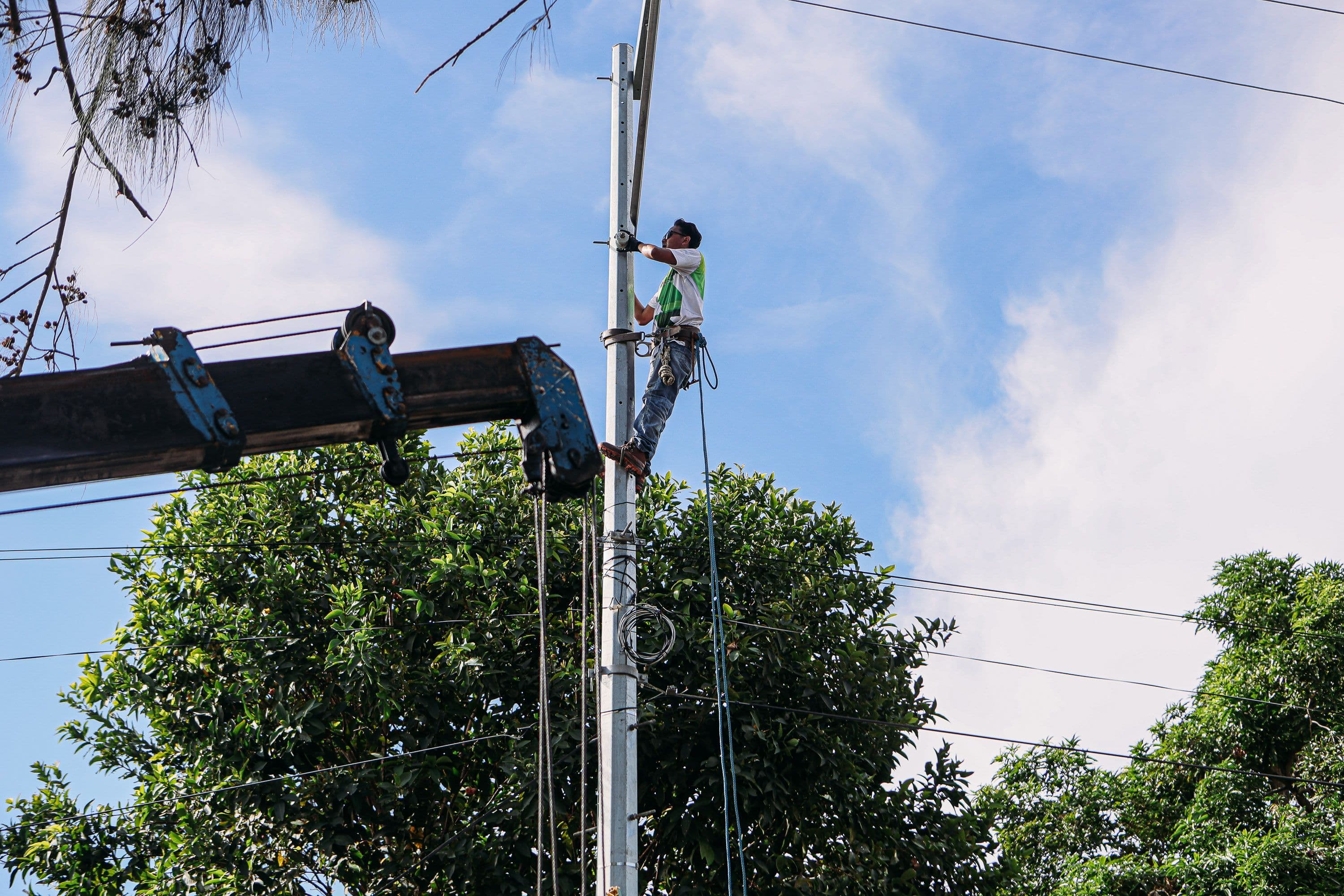 A utility worker climbs a pole for maintenance under a clear sky, showcasing safety and skill.