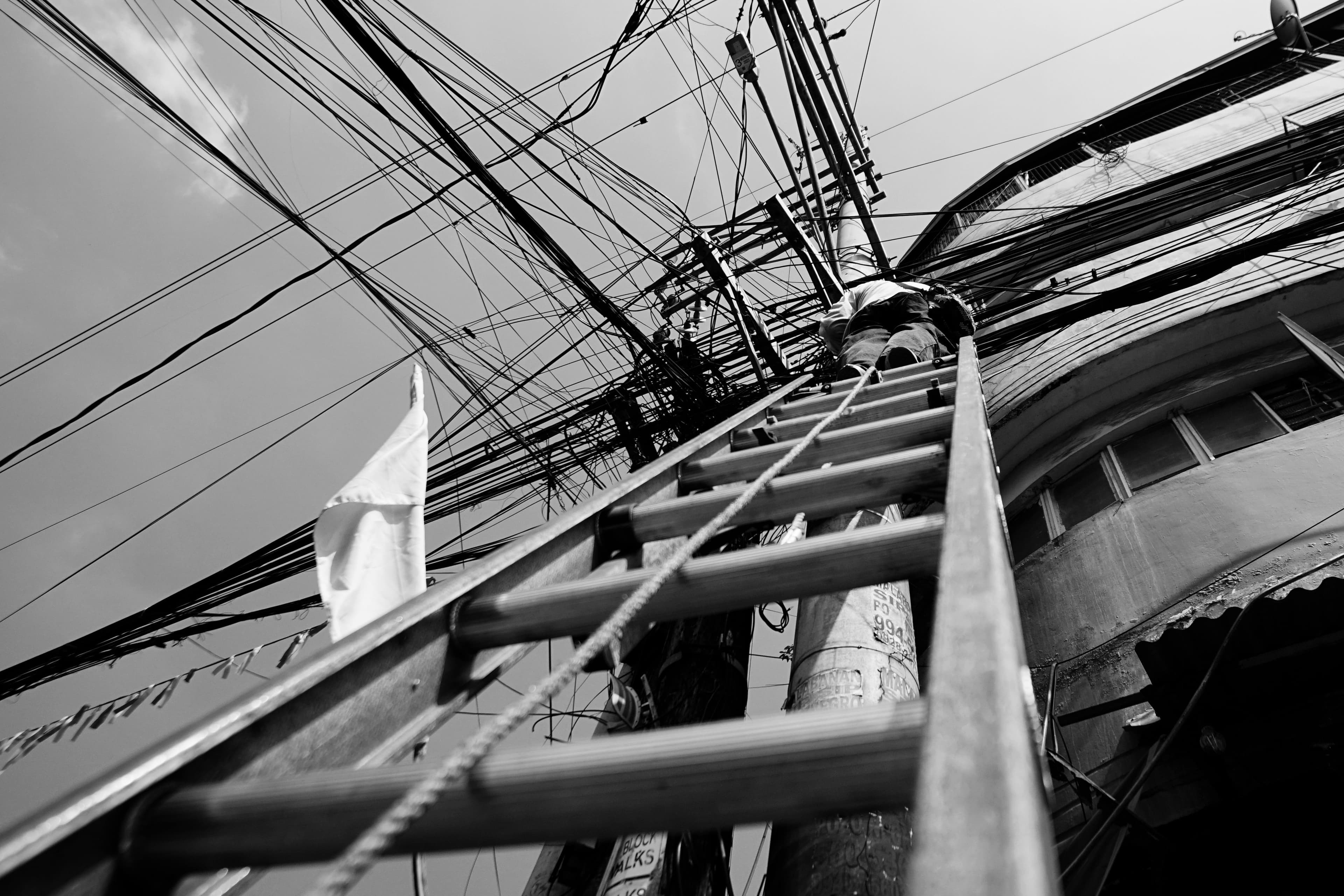 Black and white photo of a technician climbing a ladder to repair power lines outdoors.