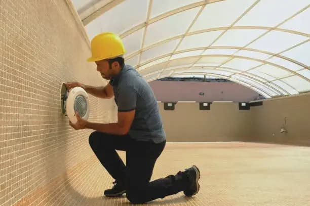 Electrician with screwdriver fixes light bulb in an empty swimming pool under construction.