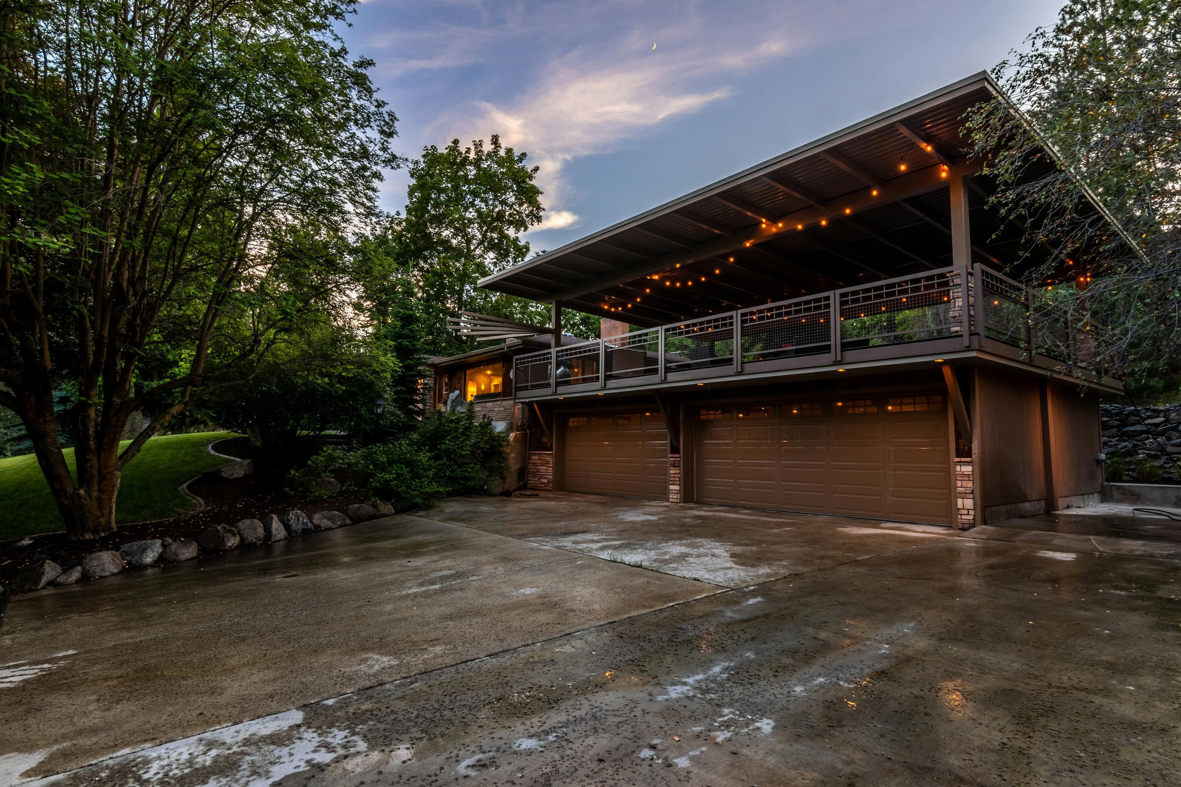 Spacious modern home's exterior with string lights illuminating a twilight setting, featuring lush greenery.