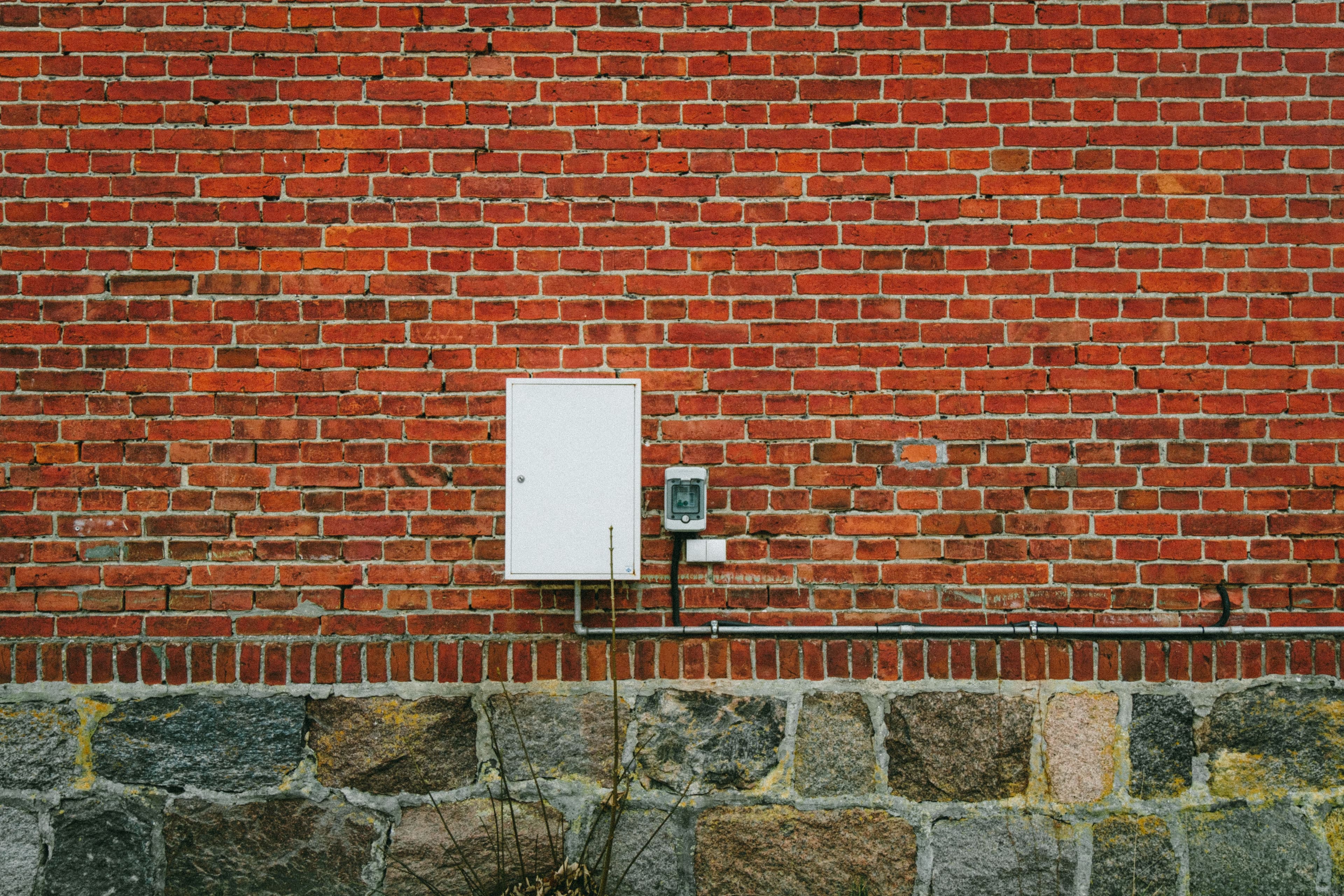 A textured red brick wall with an electric meter box, captured outdoors in Poland.