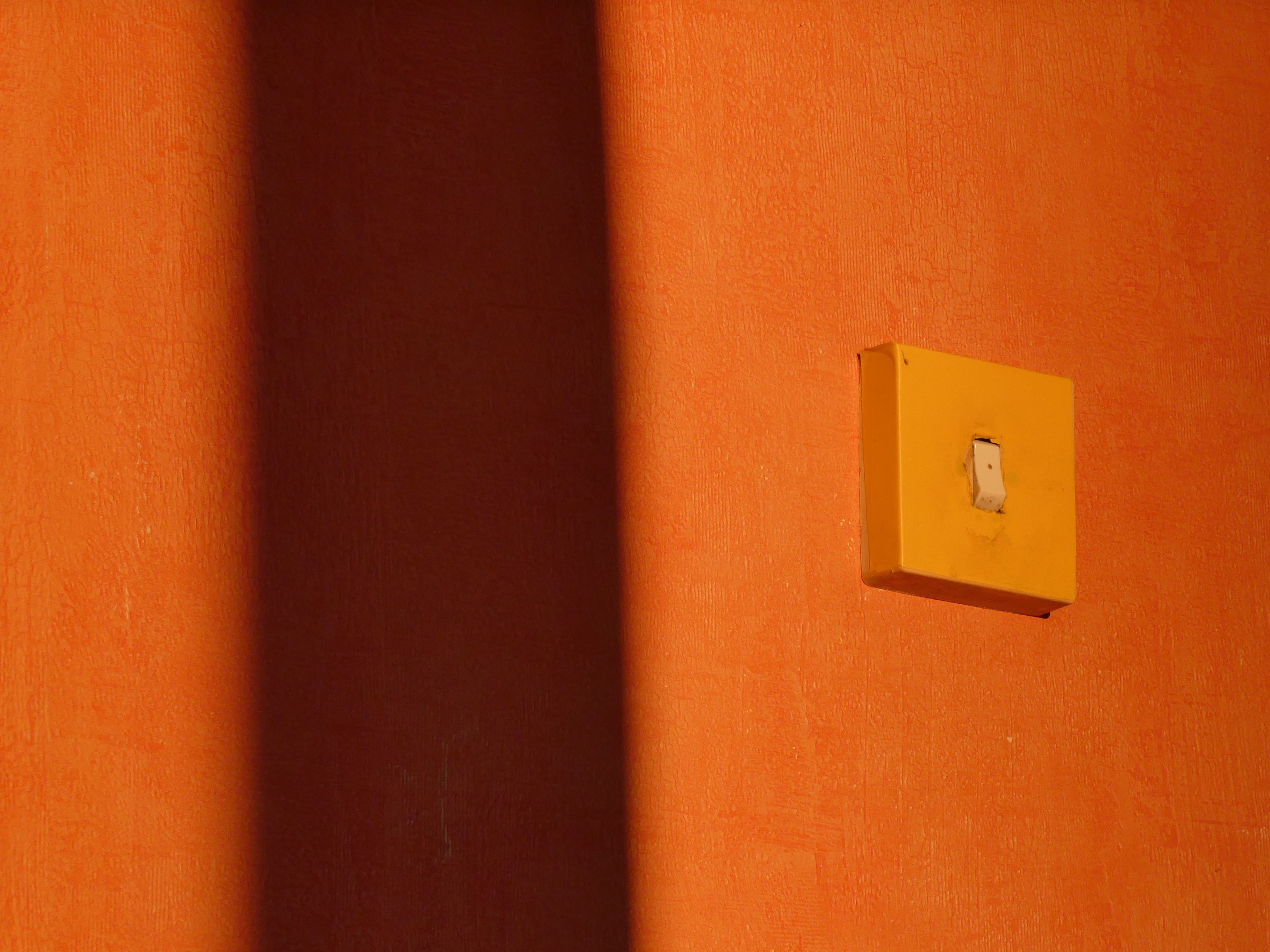 Minimalist image showcasing a light switch casting shadows on a vibrant orange wall.