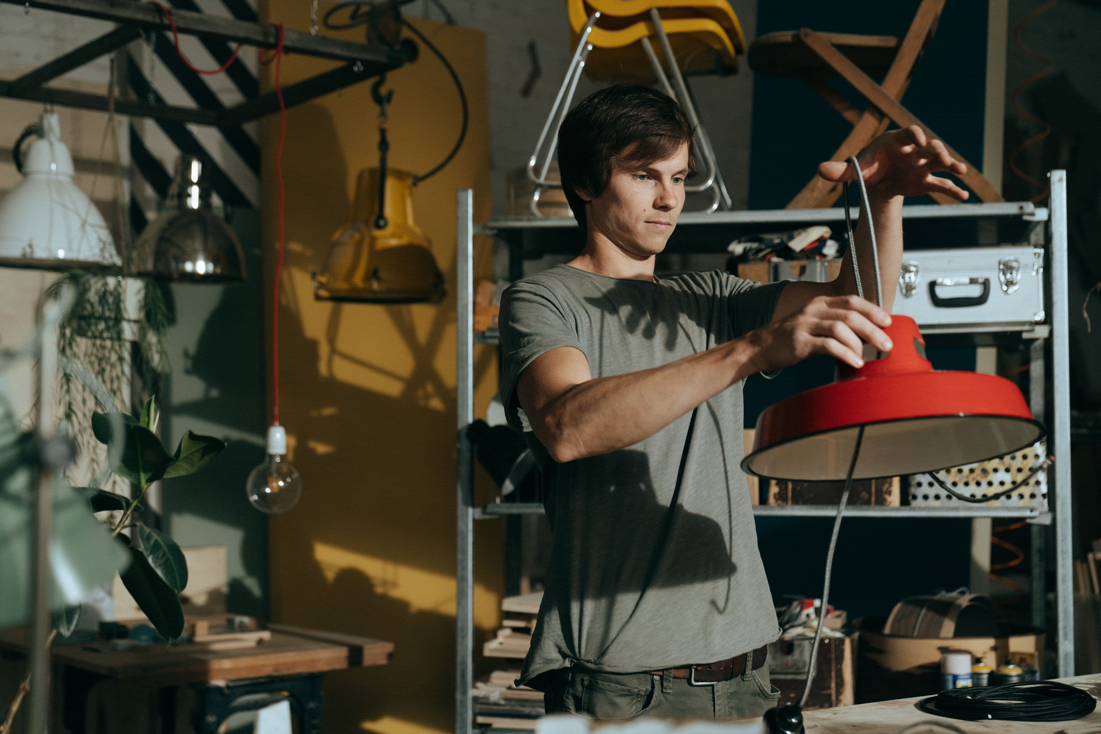 A man working indoors repairing a red lamp in a craft workshop environment.