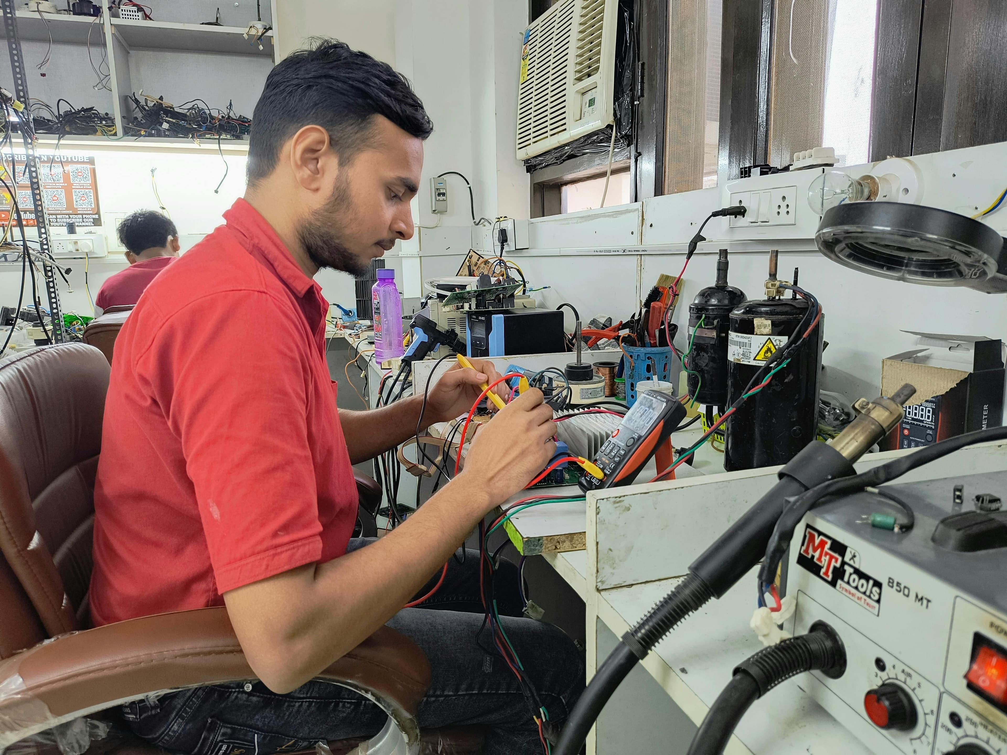 A young technician repairing electronics at a workshop. Focus on concentration and skill.