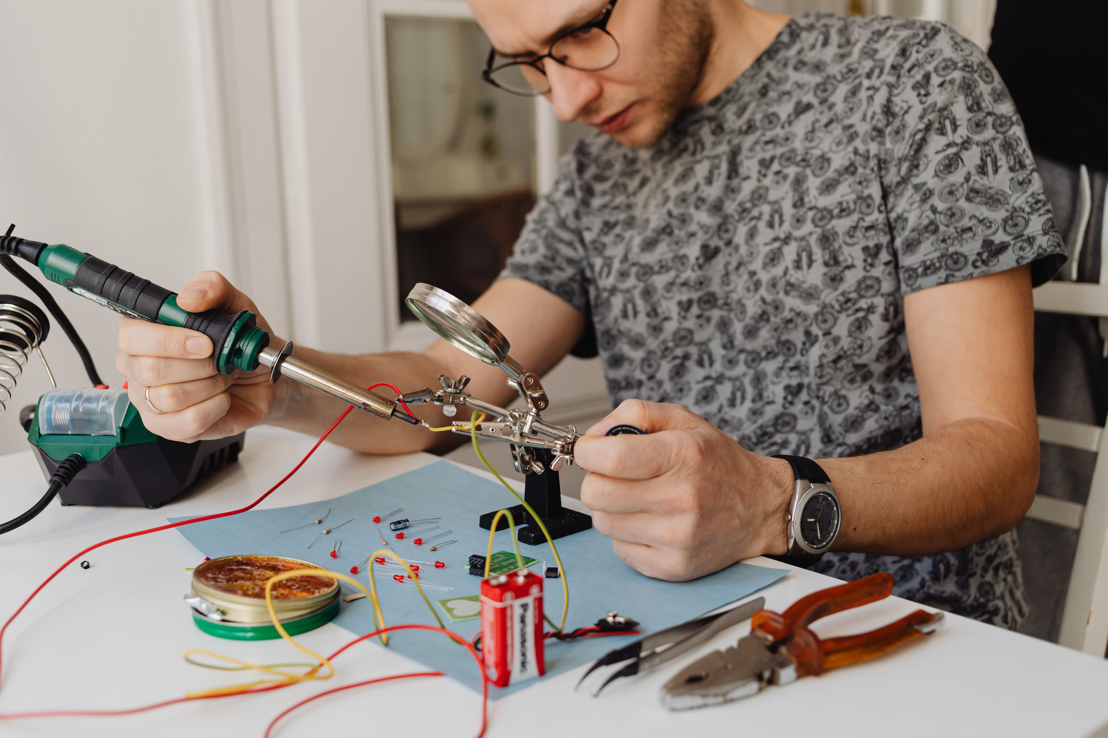 Adult technician soldering electronics with precision tools and equipment indoors.
