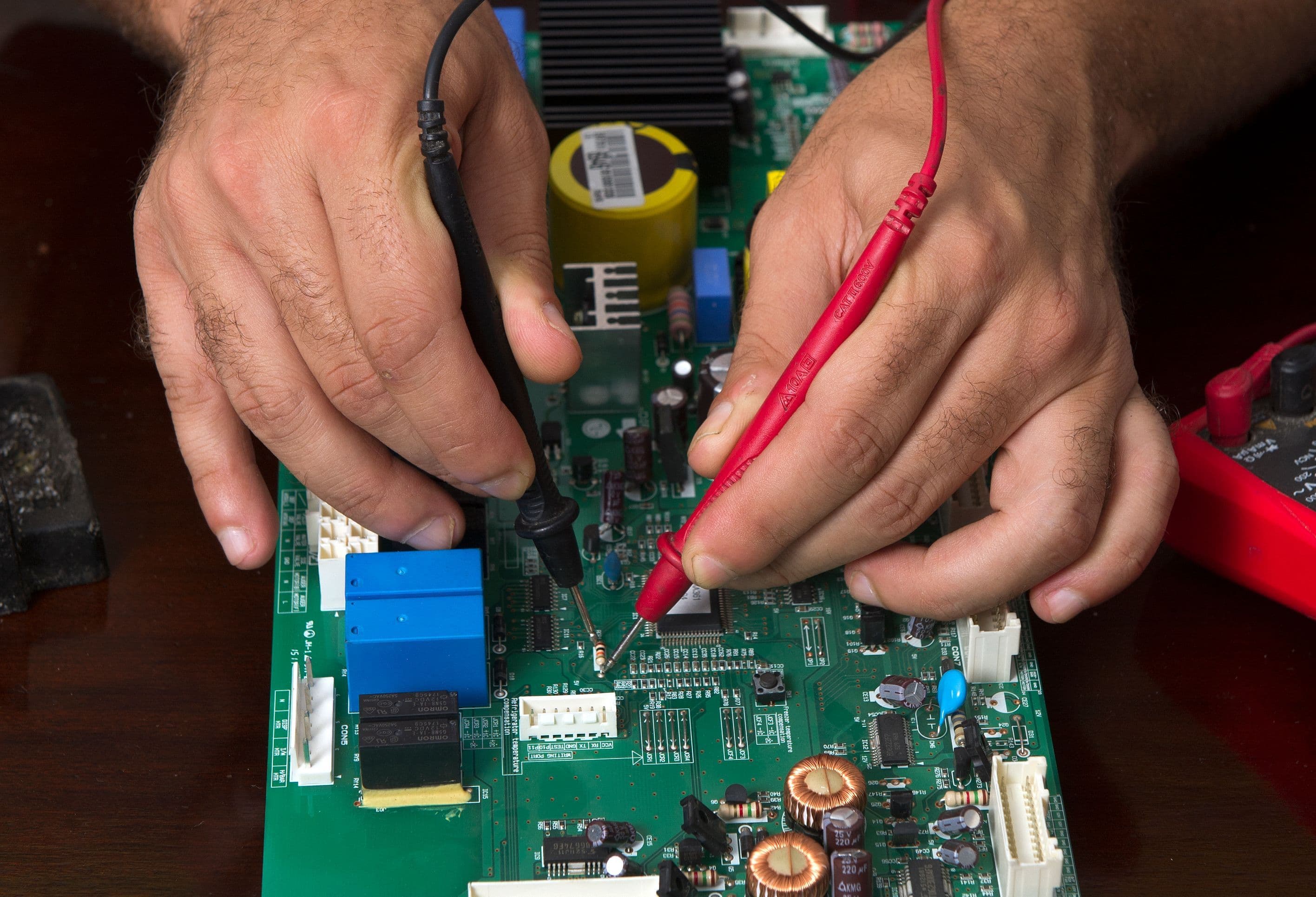 A detailed view of hands working on a circuit board using probes, depicting precision and electronics repair.
