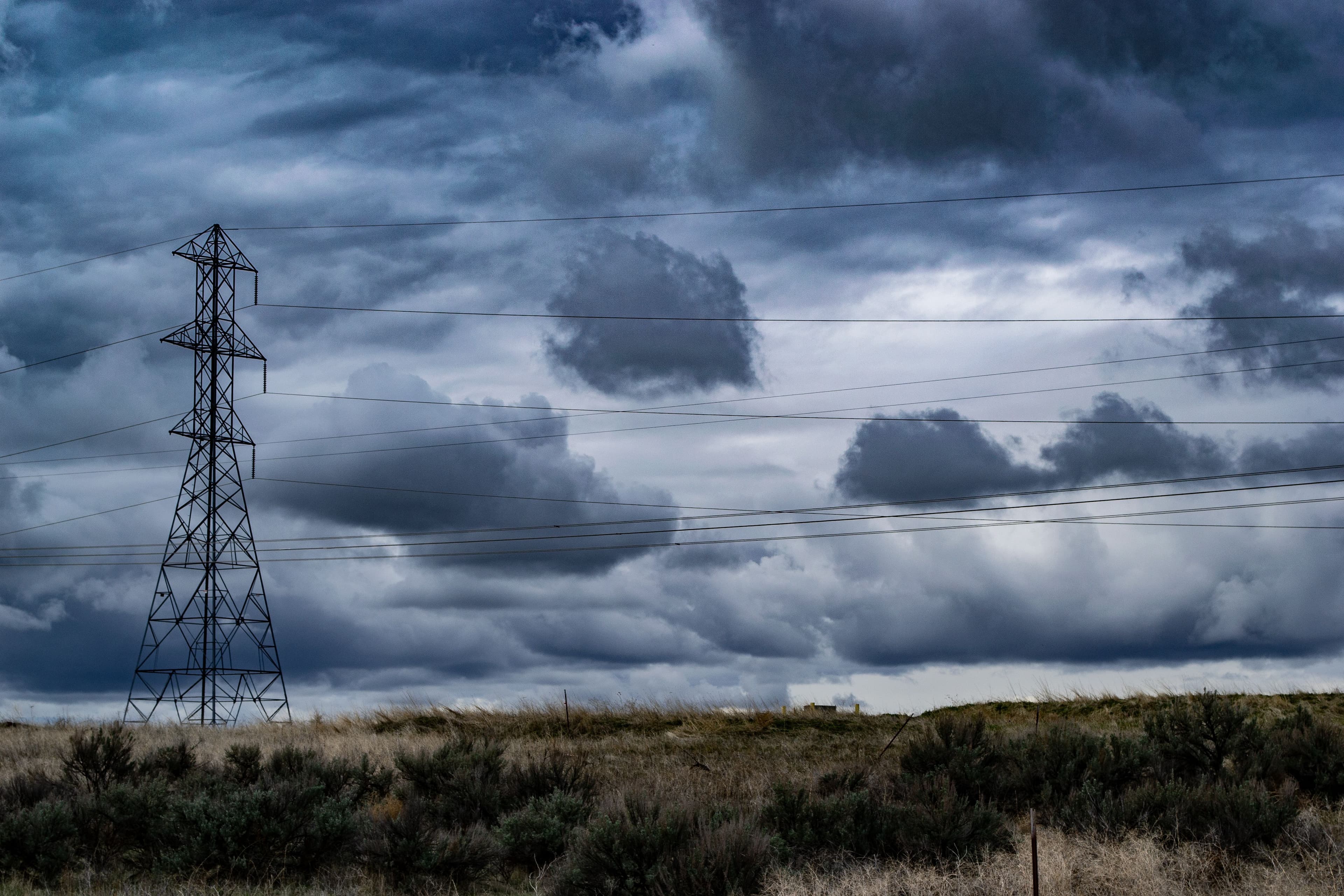 A dramatic stormy sky dominates over a field intersected by towering power lines.