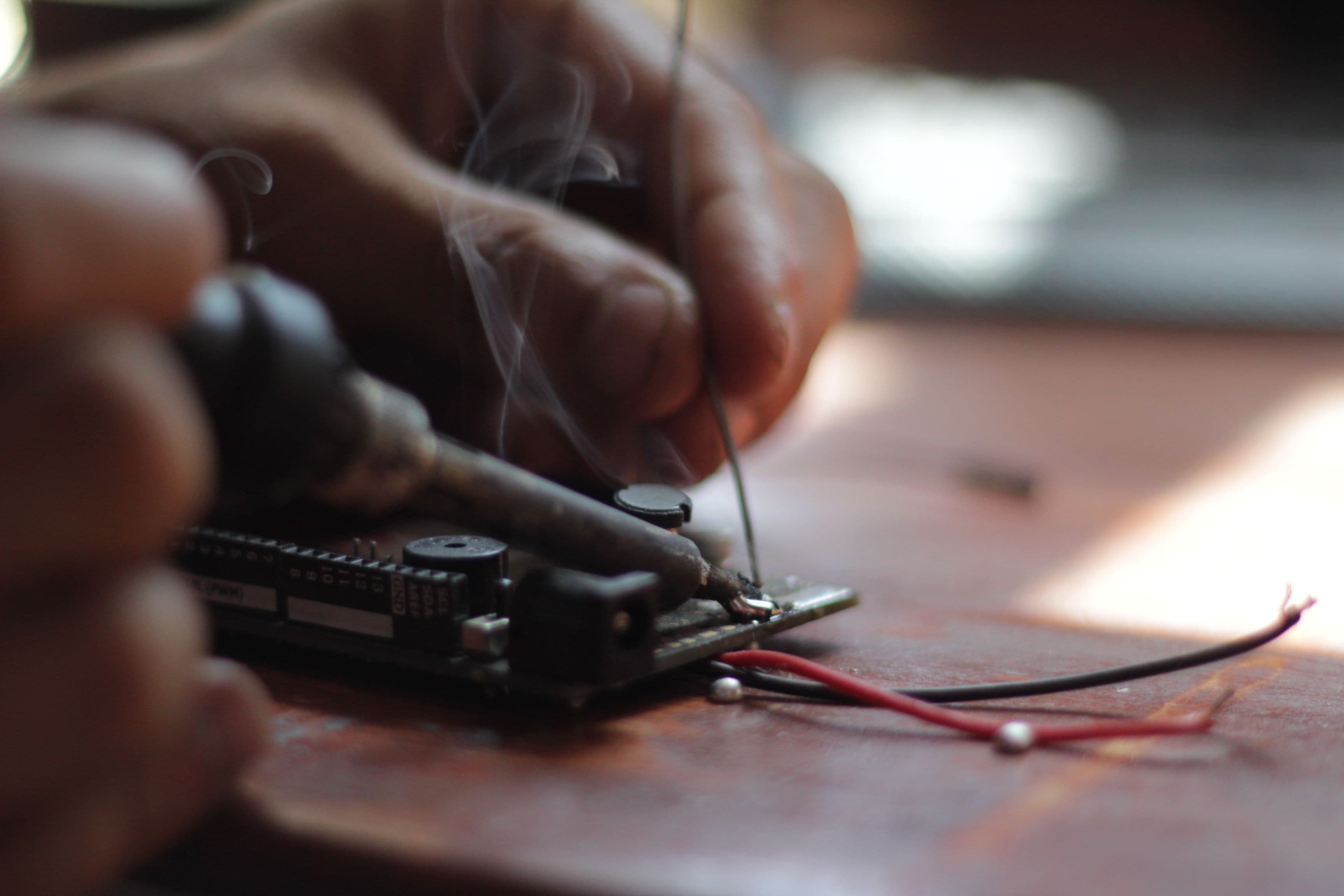 Detailed view of soldering process with visible smoke on an electronic circuit board, emphasizing precision.